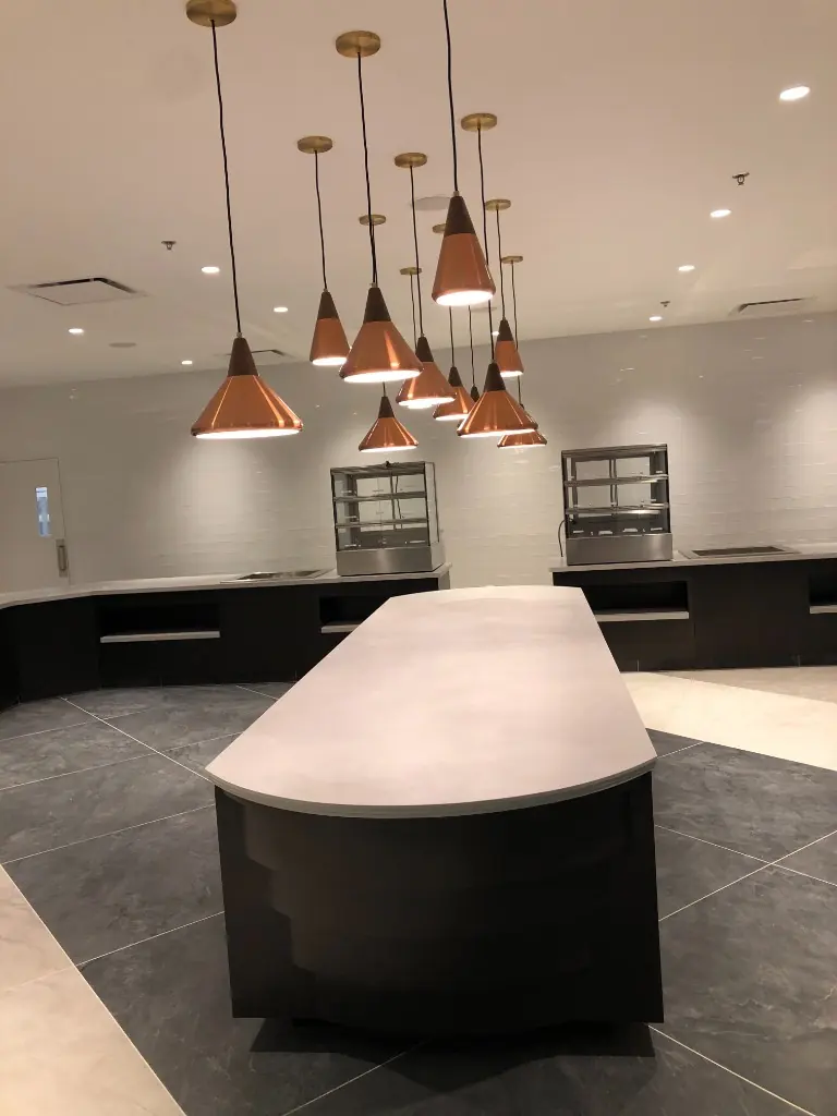 Commercial Kitchen Island Millwork | Warm Home Inc Commercial serving island with dark casework, stone top, and copper pendant lighting by Warm Home Inc