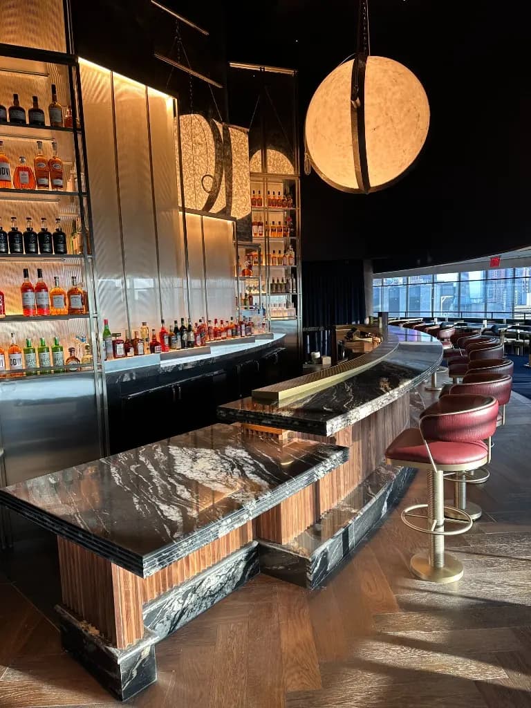 Hospitality Bar Millwork | Warm Home Inc Luxury hospitality bar with black marble counter, wood-slat base, and backlit bottle millwork by Warm Home Inc