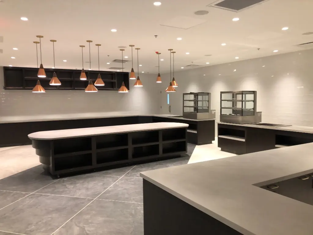Cafeteria Serving Millwork | Warm Home Inc Commercial cafeteria kitchen with dark wood island, subway tile, and custom serving millwork by Warm Home Inc