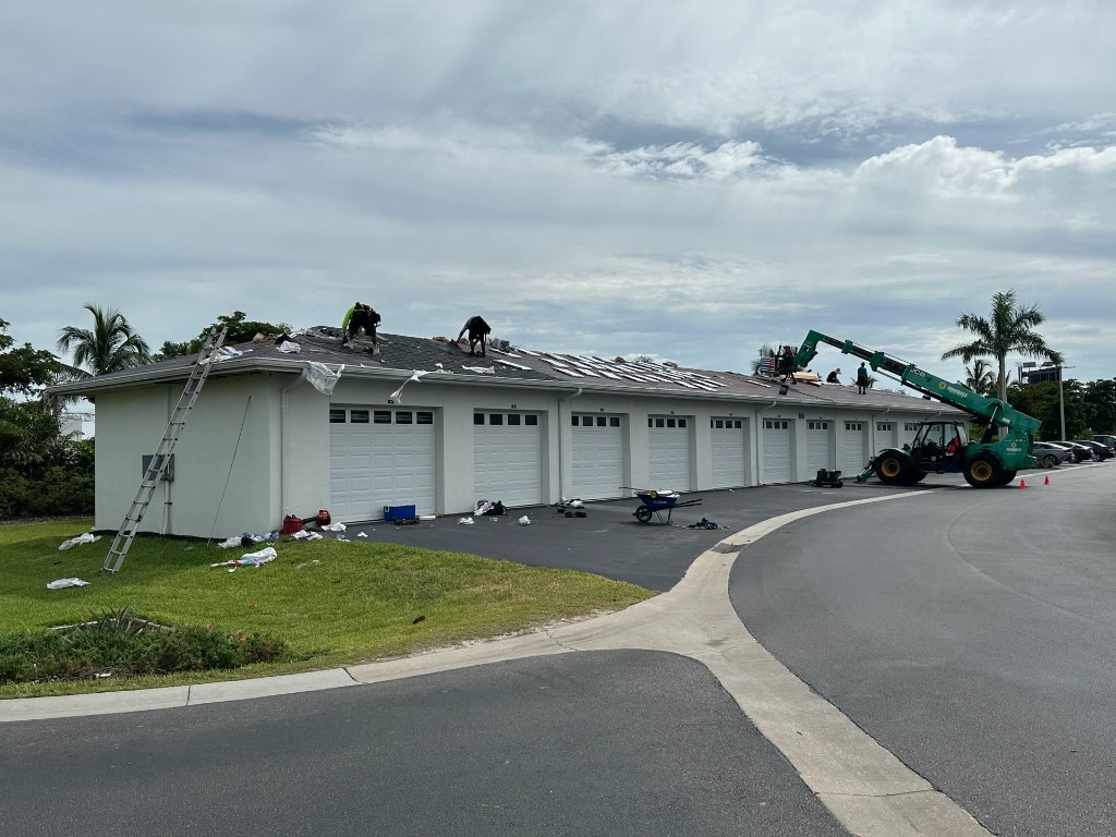 fl-fort-myers-garage-row-1.jpg Fort Myers single-story garage row with crew on a dark shingle roof and a telehandler at the drive