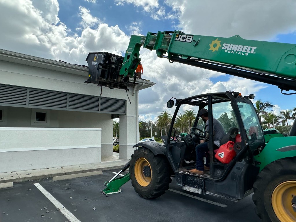 fl-fort-myers-telehandler-1.jpg Telehandler lifting a dumpster at a Fort Myers building with a crew member on the roof